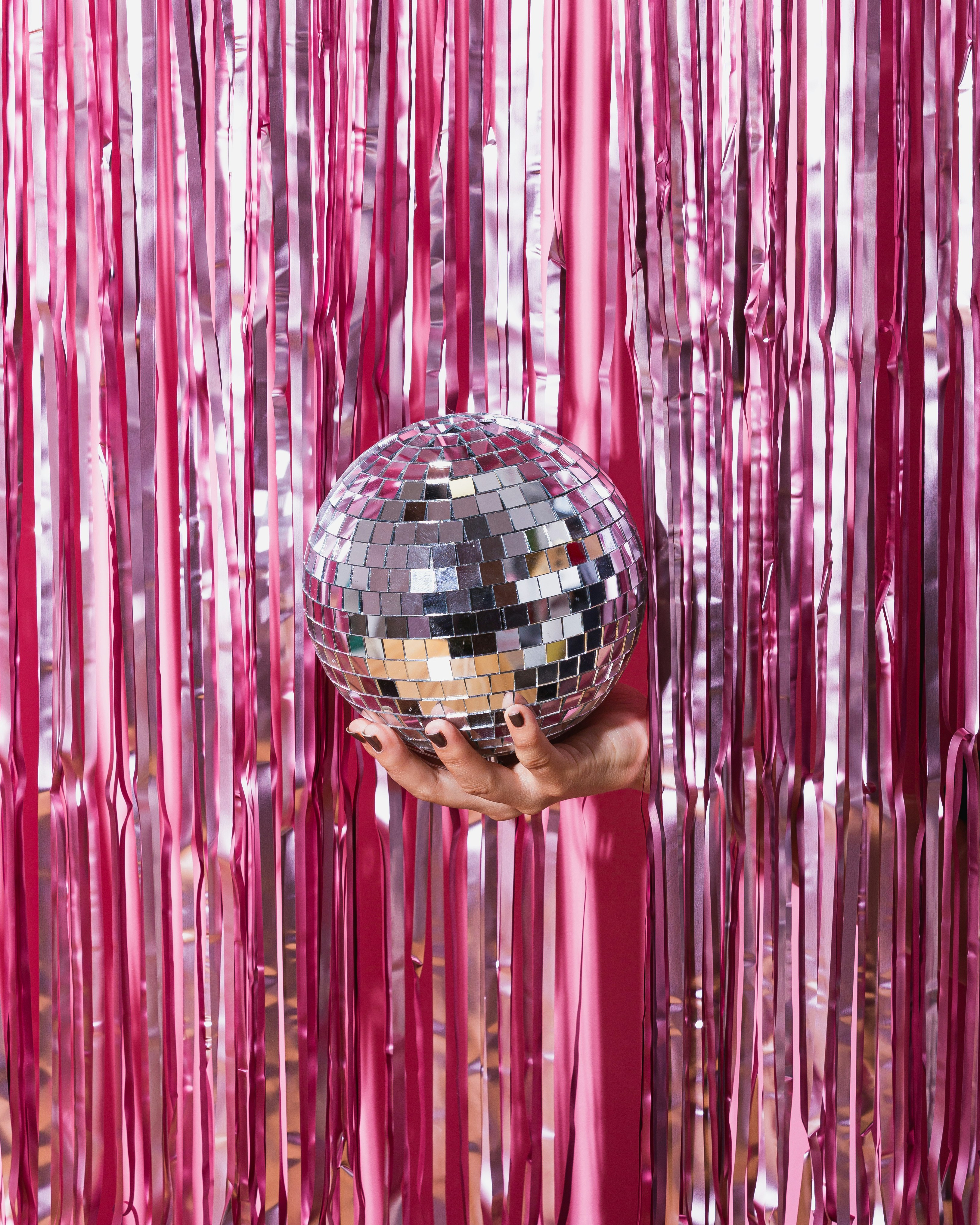 foto på ett rosa draperi, ut från draperiet håller en hand i en discokula.