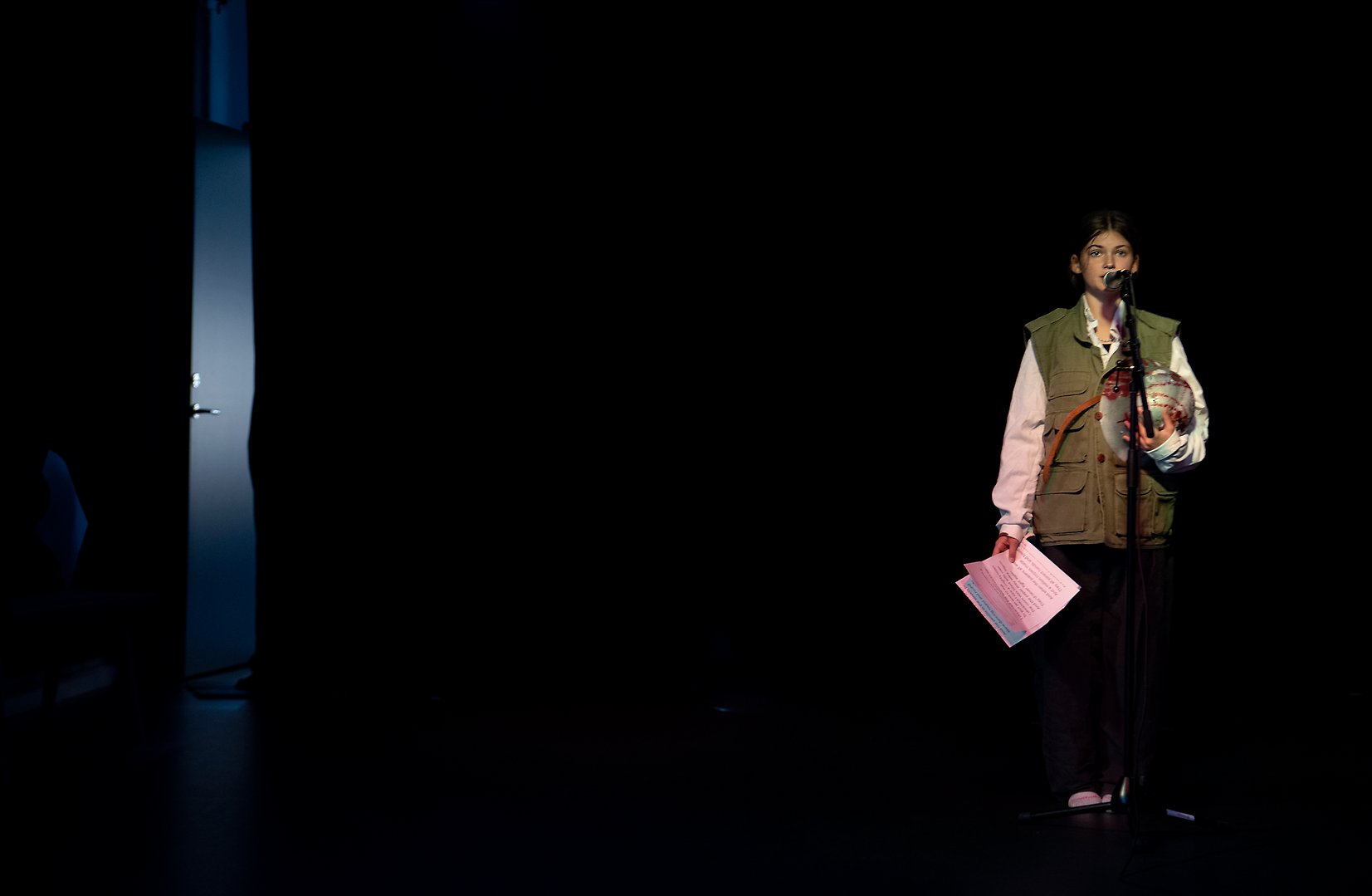 Foto på en elev som står ensam på en scen framför en mikrofon. 