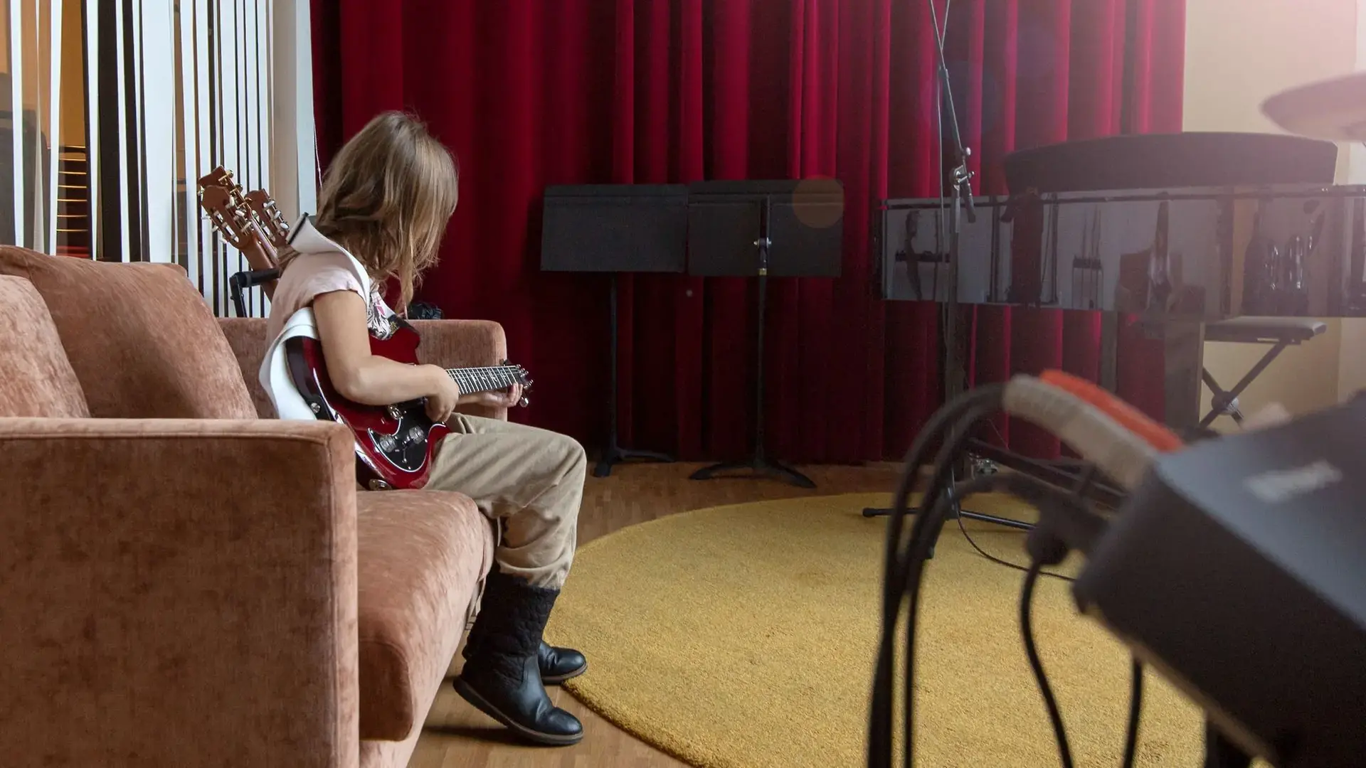 elev sitter i rosa soffa och spelar på en röd elgitarr